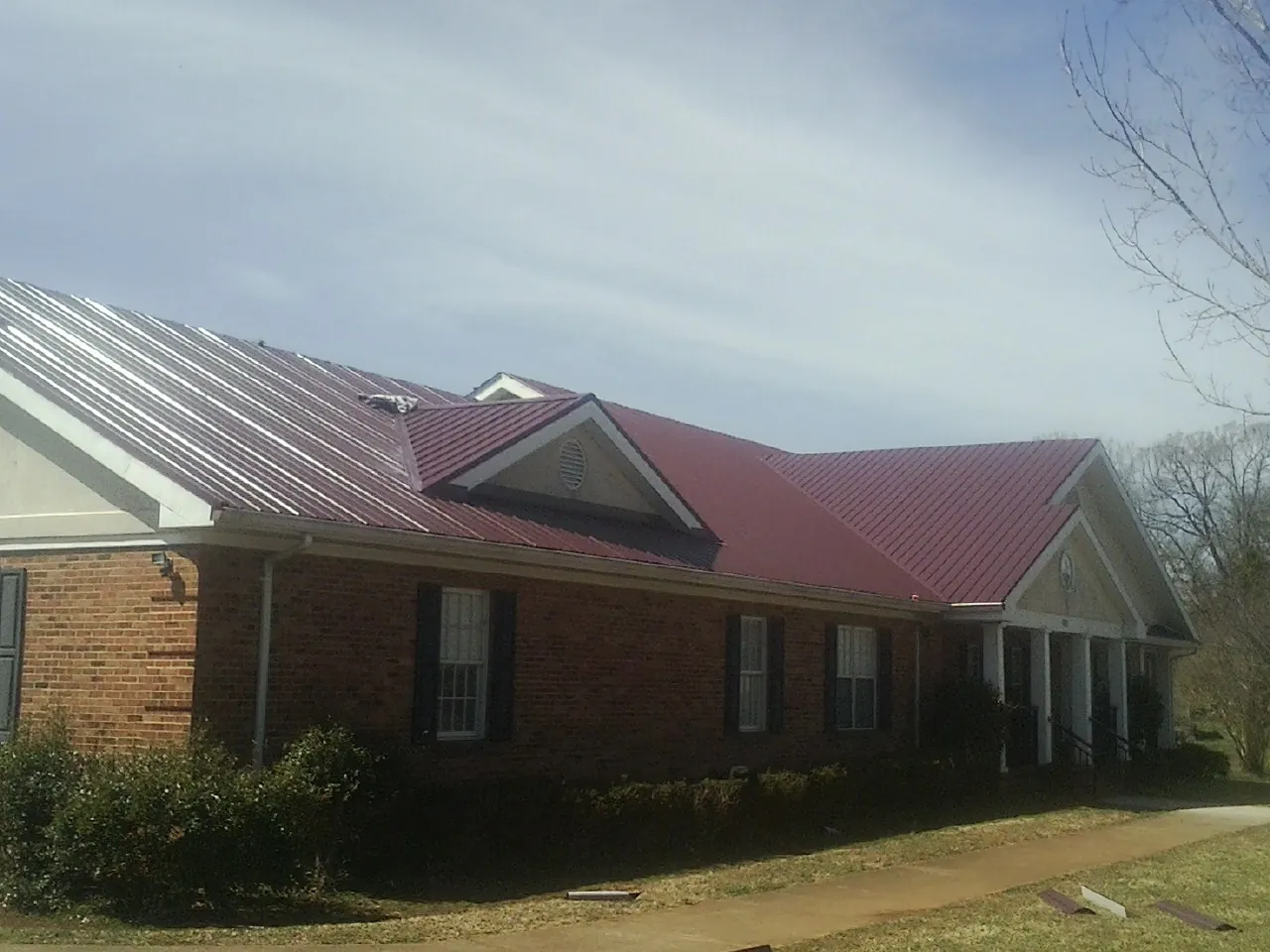 Red metal roof with gabled entries on a long brick building, from a Hail Damage Roof Repair job in Leonardsville