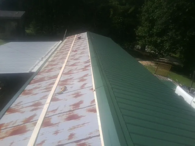 Old rusted panels beside newly installed green metal roofing — Wind Damage Roof Repair by Roofing Brothers in Leonardsville