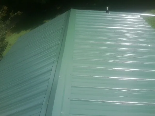 New green metal panels meeting at the ridge of a roof — Flat Roof Repair work by our crew in Leonardsville