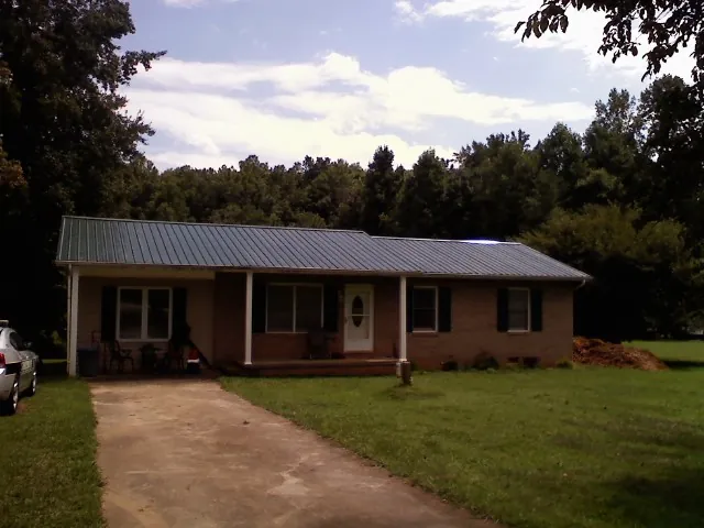 Dark green metal roof on a brick ranch with a covered porch in Leonardsville