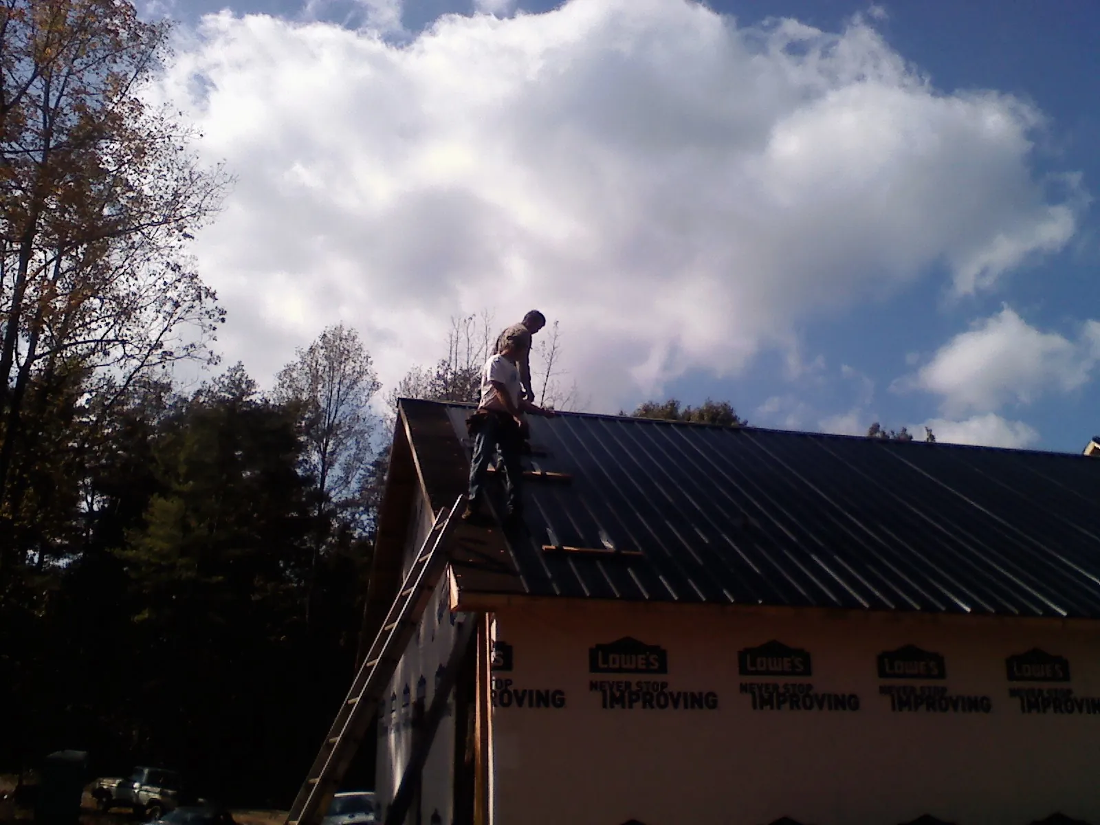 Roofer fastening dark metal panels high against a cloudy sky, from a Roof Inspection job in Leonardsville