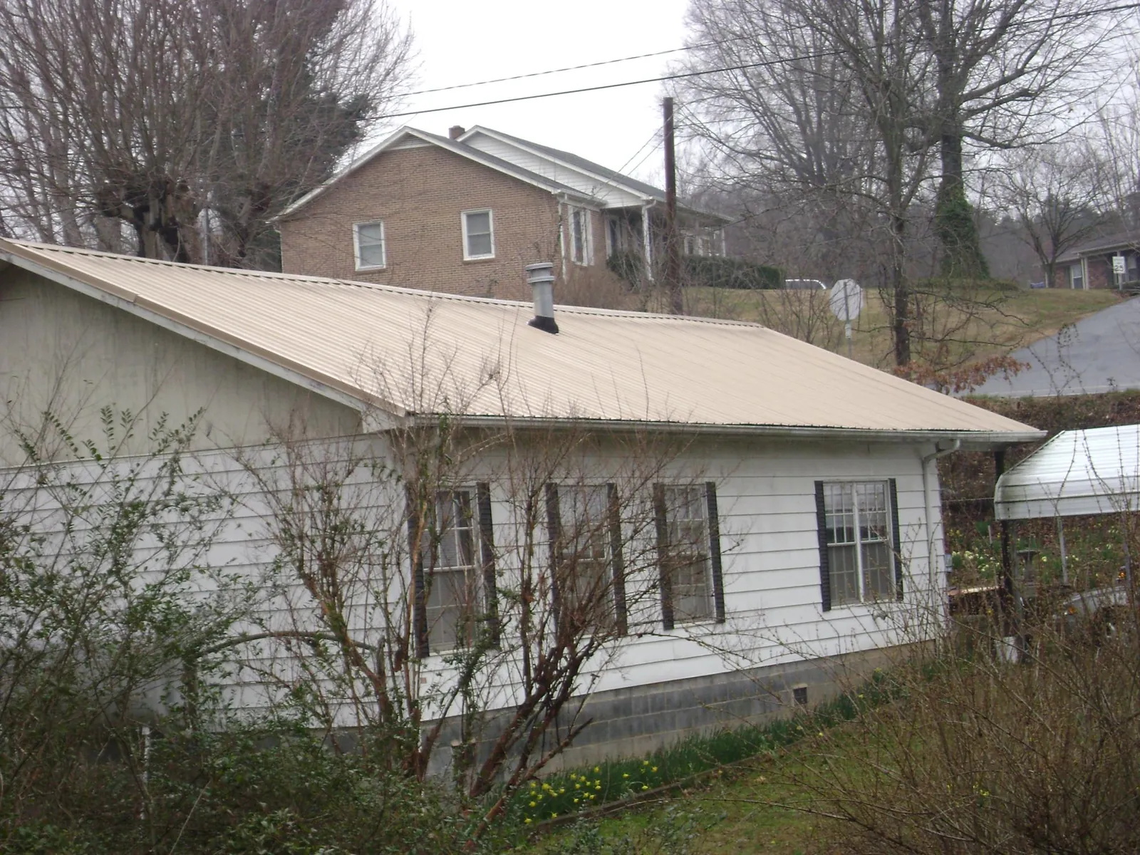 Tan metal roof on a white sided house set into a hillside — Commercial Roofing by Roofing Brothers in Leonardsville