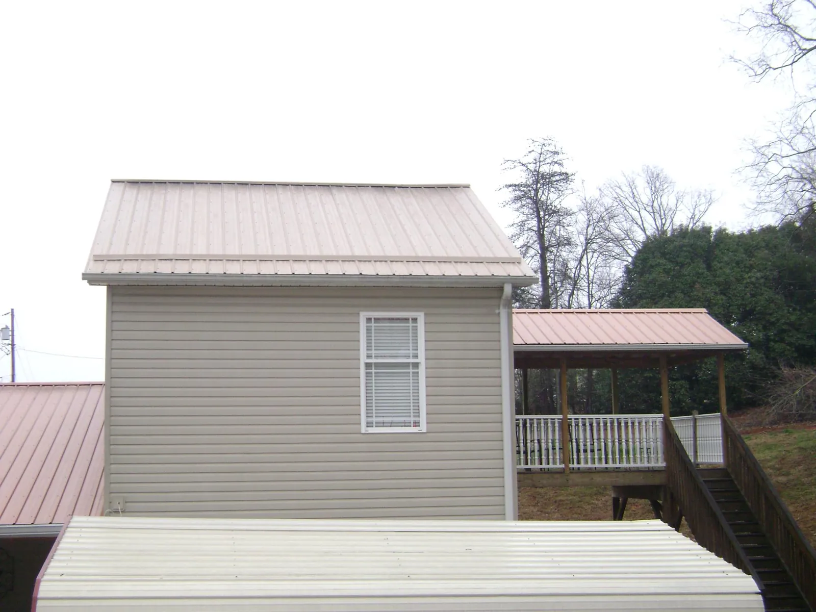 Tan metal roofs on a two story addition and attached porch, from a Roof Replacement job in Leonardsville
